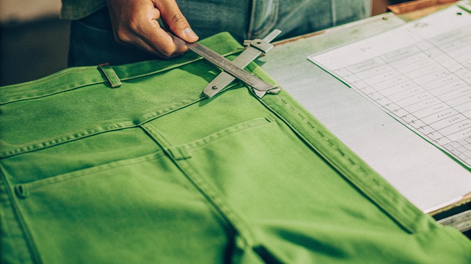 Measuring Jeans Quality with AQL and On-Time Delivery Metrics A quality control inspector's hands using a caliper to measure a jean's waistband, with a checklist and AQL chart nearby.