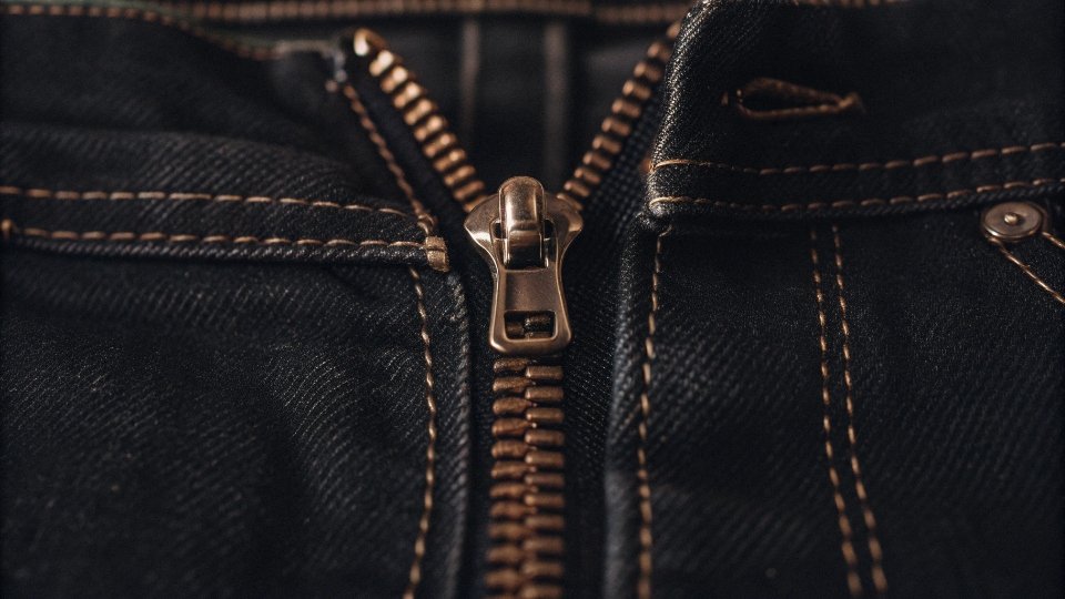 Custom Jean Zippers A close-up of a high-quality brass zipper on a pair of dark wash denim jeans