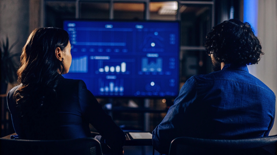 Account Performance Reviews with Factory Two people in a meeting, reviewing a performance dashboard with charts and graphs.