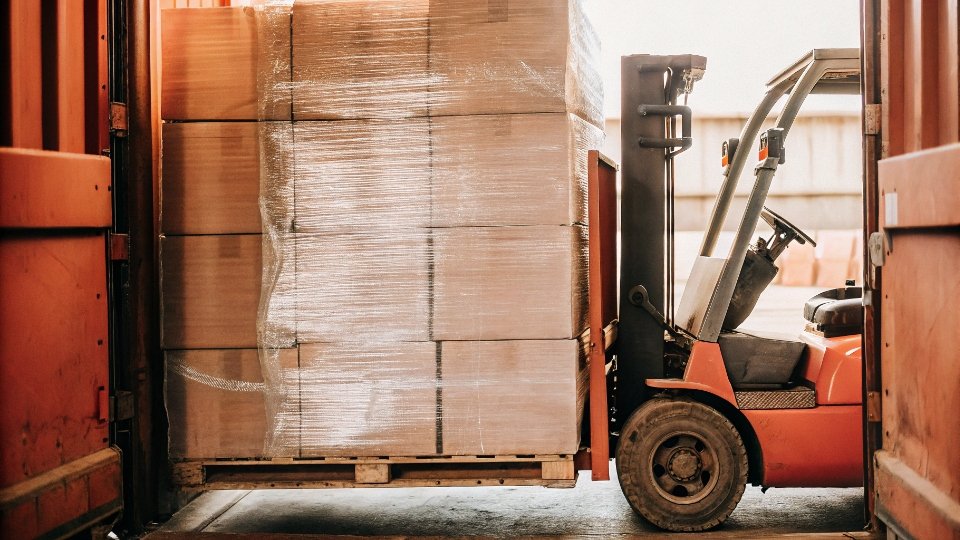 Optimized Palletizing for Jeans Freight Cost Reduction A perfectly stacked and shrink-wrapped pallet of cartons being loaded into a shipping container with a forklift.
