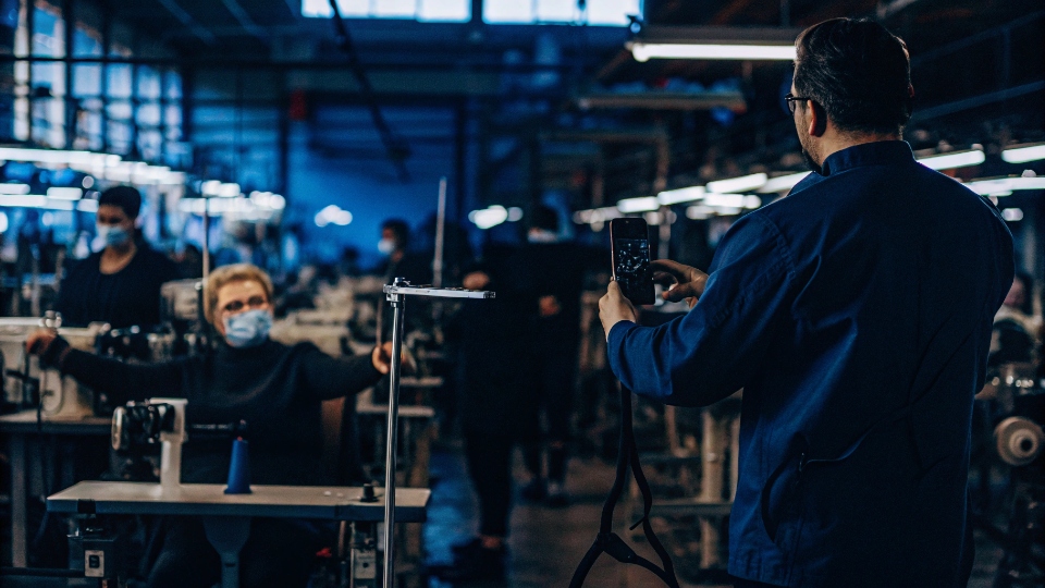 A factory manager holding a smartphone to livestream a sewing station