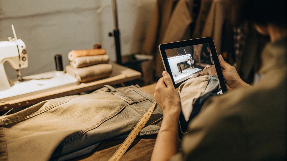 Guidance for Local Jean Hardware Repair A tailor watching a video tutorial on a tablet while expertly replacing a rivet on a pair of jeans.