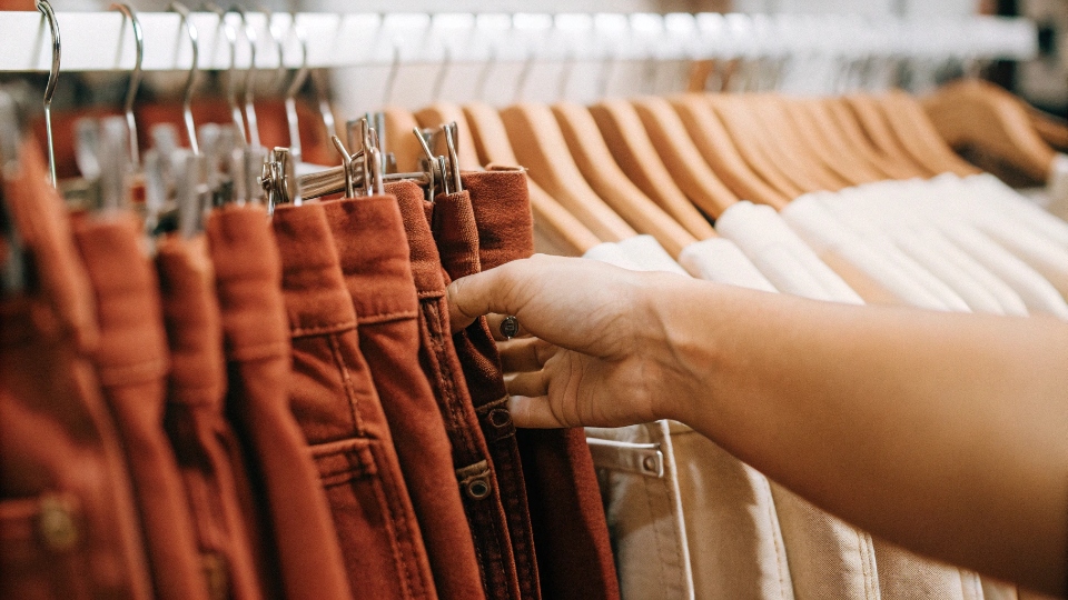 Small Batch Pilot Run of 50 Jeans A hand selecting one pair of jeans from a small boutique rack holding about 50 pairs.