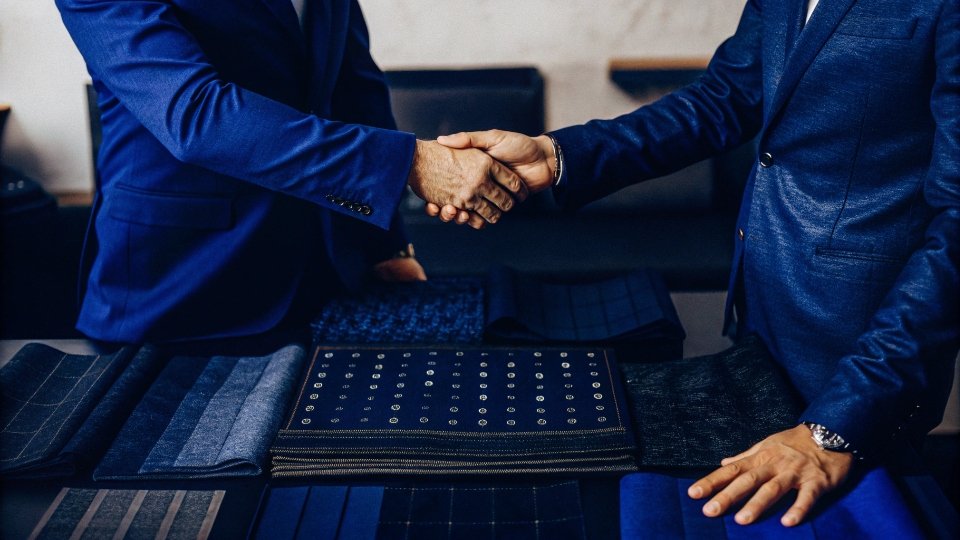 Negotiating Multi-Season Price Holds on Materials Two people shaking hands over a table with fabric swatches and a multi-season calendar.