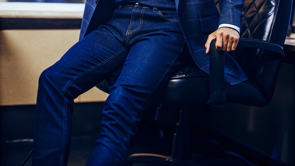 A person in a modern office wearing dark jeans, a blazer, and dress shoes.