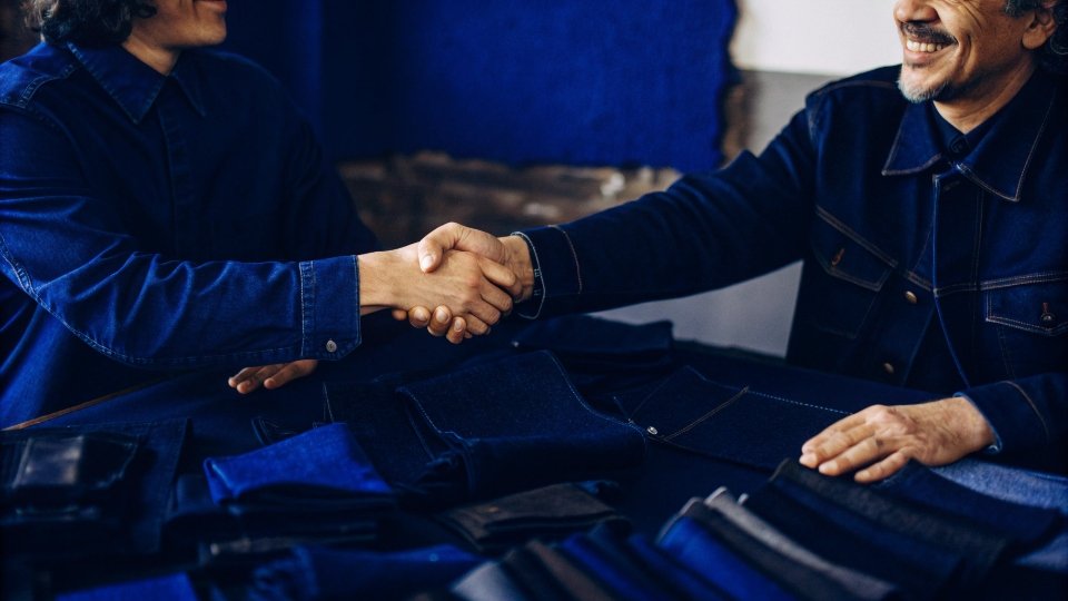 Co-Investing in Bespoke Wash Processes Two people, a designer and a factory manager, shaking hands over a table of denim swatches.