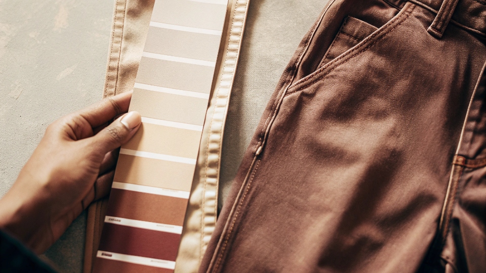 Pantone Color Matching for Custom Jeans A hand holding a Pantone color swatch next to a piece of perfectly matched custom dyed denim