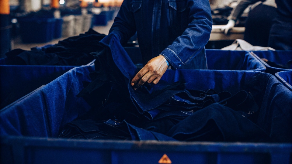 Separating and Storing Fabric Off-Cuts A factory worker carefully separating large denim off-cuts from the cutting table and placing them in a designated bin.