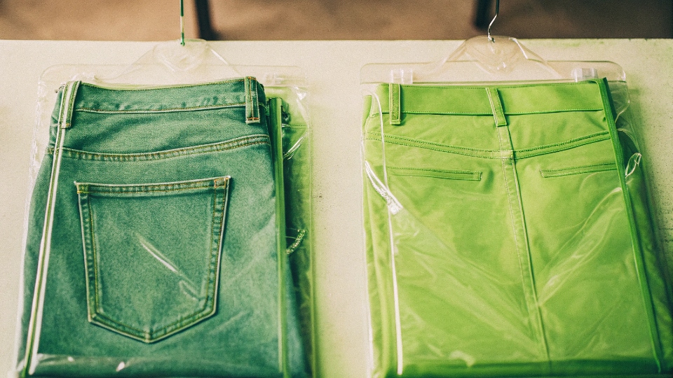 Folded Polybag vs. Hanger-Ready Jeans Packaging A neatly folded jean in a clear polybag next to a jean on a branded hanger, protected by a long plastic cover.