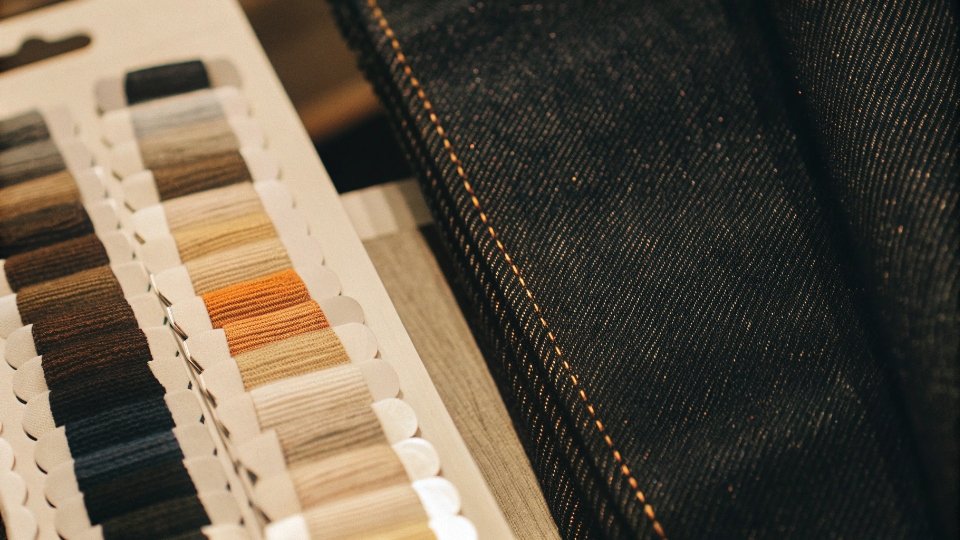 Customizing Thread Color for Jeans A thread color card showing hundreds of shades next to a denim fabric swatch with bright orange contrast stitching