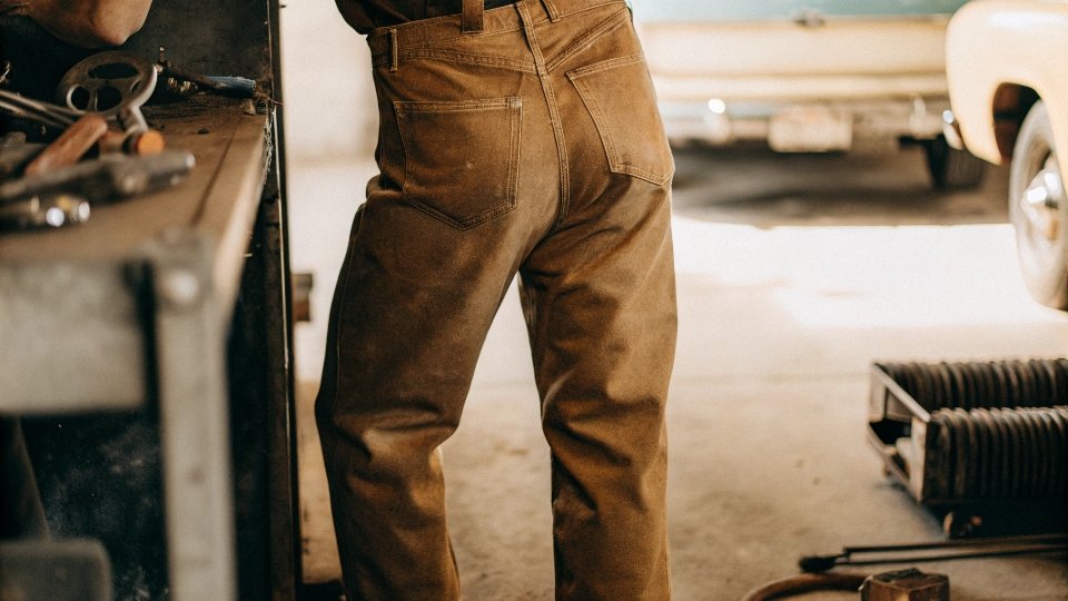 Durability of Rustler Jeans A person wearing a slightly faded but intact pair of Rustler jeans while doing some work in a garage.