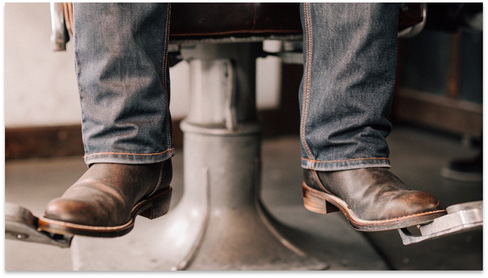 The Functional Fit of Heritage Jeans Over Boots A close-up shot of a pair of classic, dark-wash Wrangler jeans fitting cleanly over a pair of leather cowboy boots.