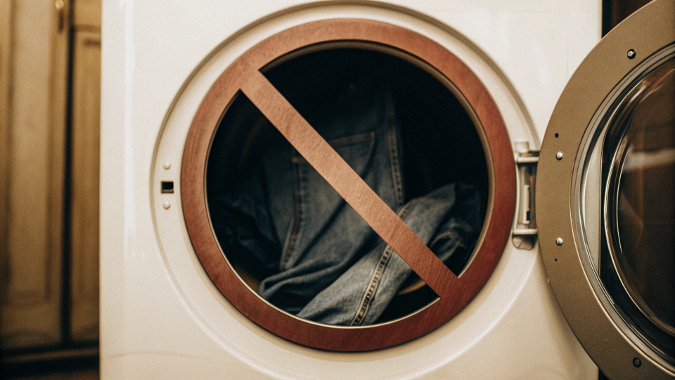 Warning Against High-Heat Drying for Jeans A warning symbol (like a red circle with a line through it) over a clothes dryer set to high heat.