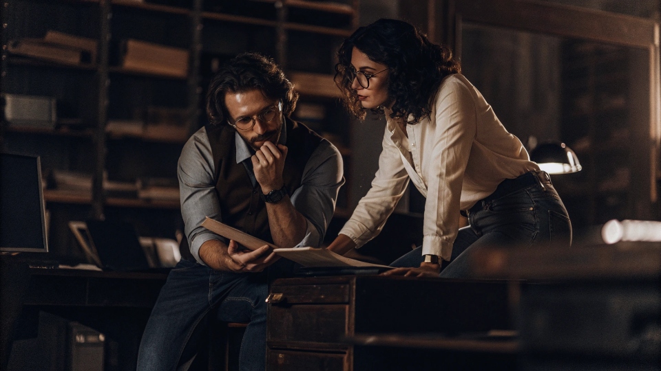 Detectives Working in Jeans A male and female detective in business casual attire, including jeans, collaborating at a desk.