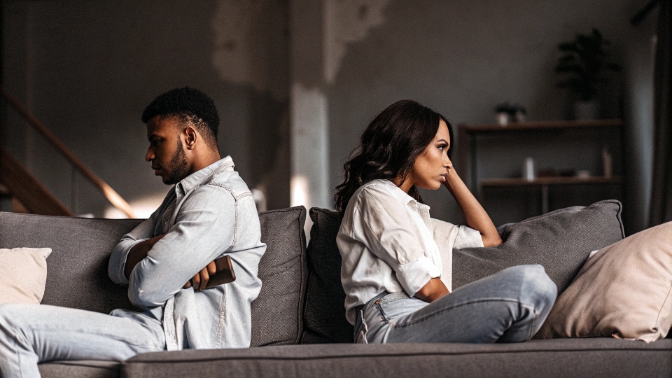 Relationship Red Flags and Emotional Distance A couple having a tense, distant conversation on a sofa, representing emotional disconnect.