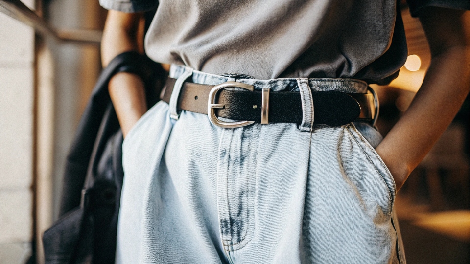 The Power of a Loose Tuck in Baggy Jeans A close-up of a person's waist, showing a t-shirt loosely tucked into high-waisted baggy jeans with a nice belt.