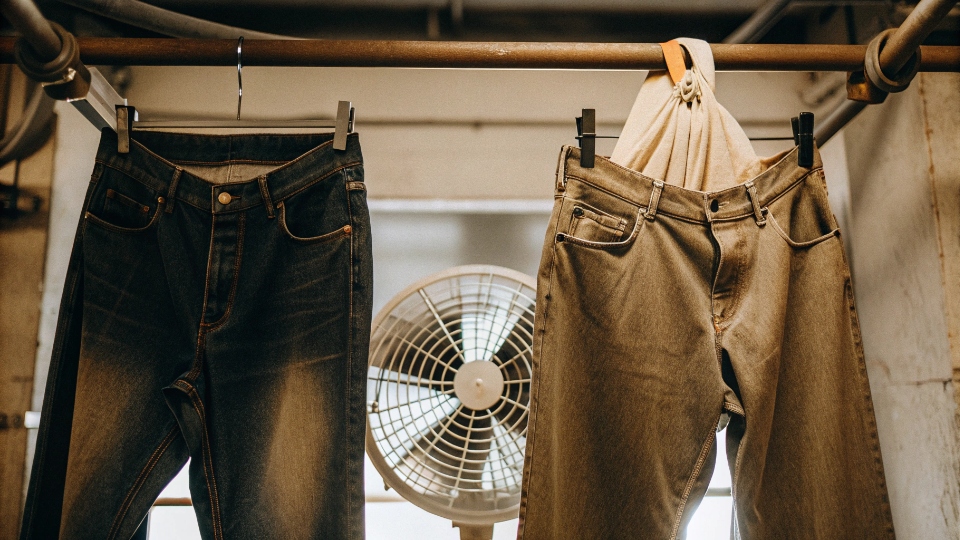 Speeding Up Jean Drying with a Fan A pair of jeans hanging indoors from S-hooks with a small floor fan pointed at them.