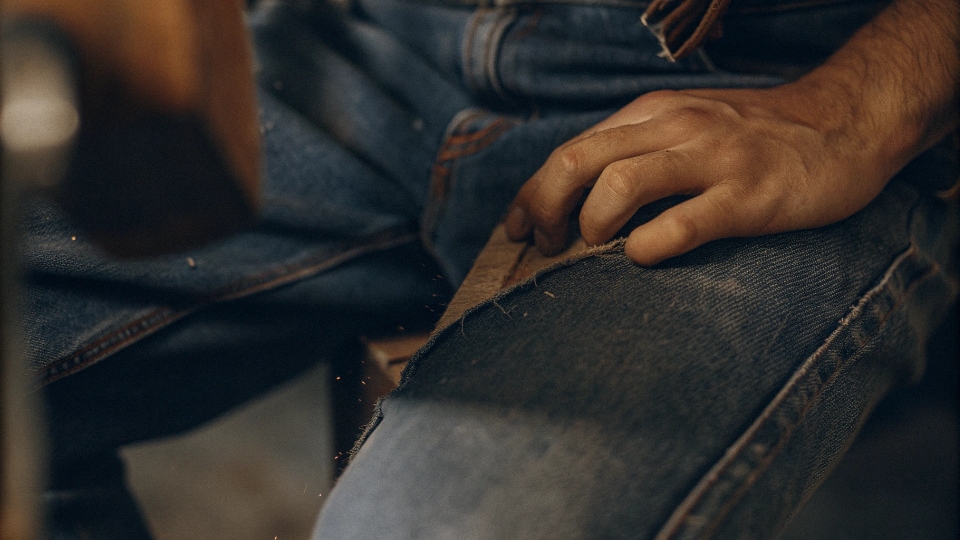 Using Sandpaper to Distress Jeans A close-up of sandpaper being rubbed on the thigh of a pair of jeans.