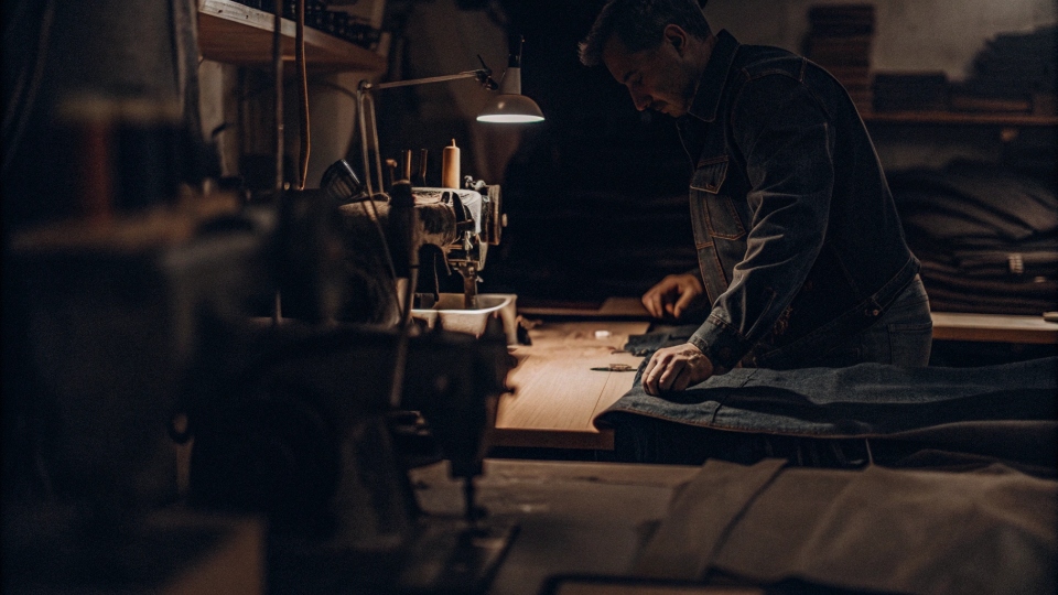 Modern USA Jean Manufacturing A denim artisan cutting fabric in a small, well-lit workshop in the USA.
