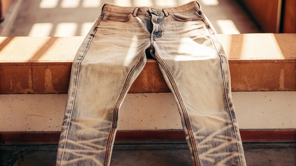 Natural Wear Patterns on Jeans A pair of well-worn raw denim jeans showing beautiful, natural fading patterns like whiskers on the lap and honeycombs behind the knees.