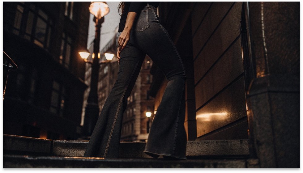 The Sculptural Silhouette of Horseshoe Jeans A woman walking down a city street wearing denim pants with a distinct curved outer seam, creating a rounded silhouette.