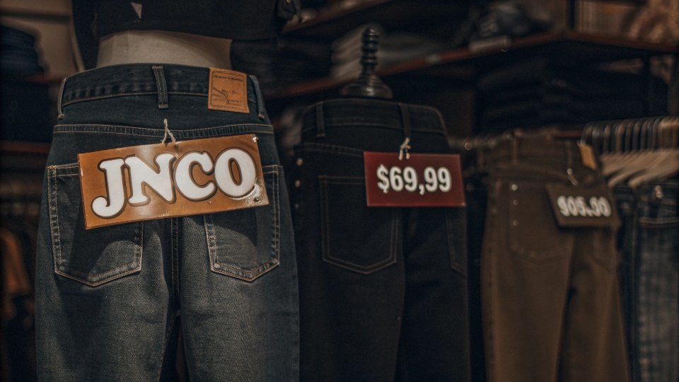 The Price of Rebellion: JNCO Jeans in the 90s A vintage 90s store display featuring several pairs of JNCO jeans with prominent price tags showing figures like $69.99.