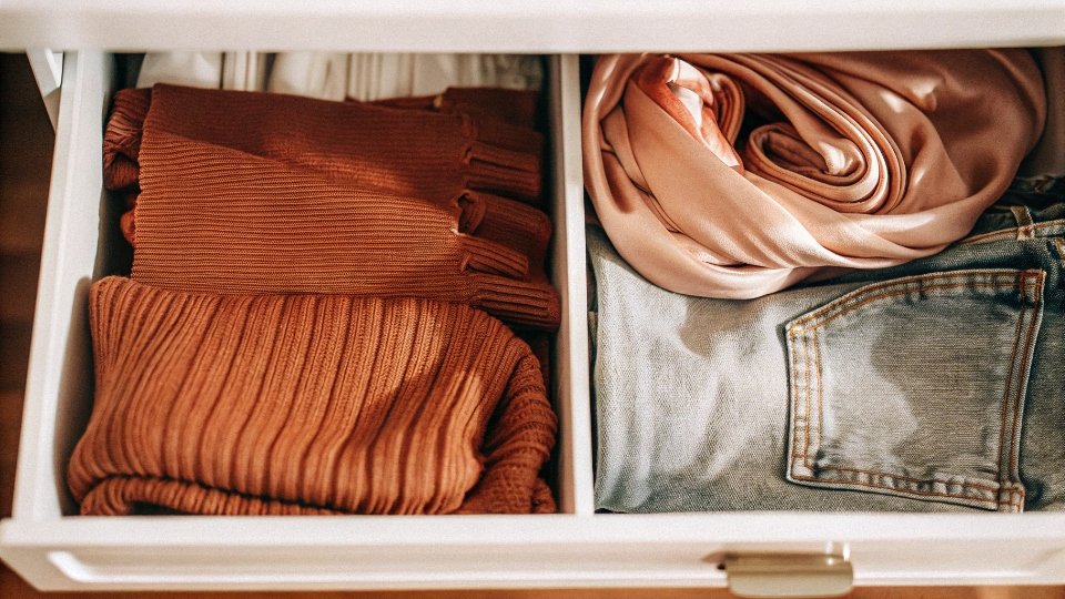 The General Trend of Freezing Clothes for Freshness An assortment of clothing items—a wool sweater, a silk scarf, and jeans—all folded inside an open freezer drawer.
