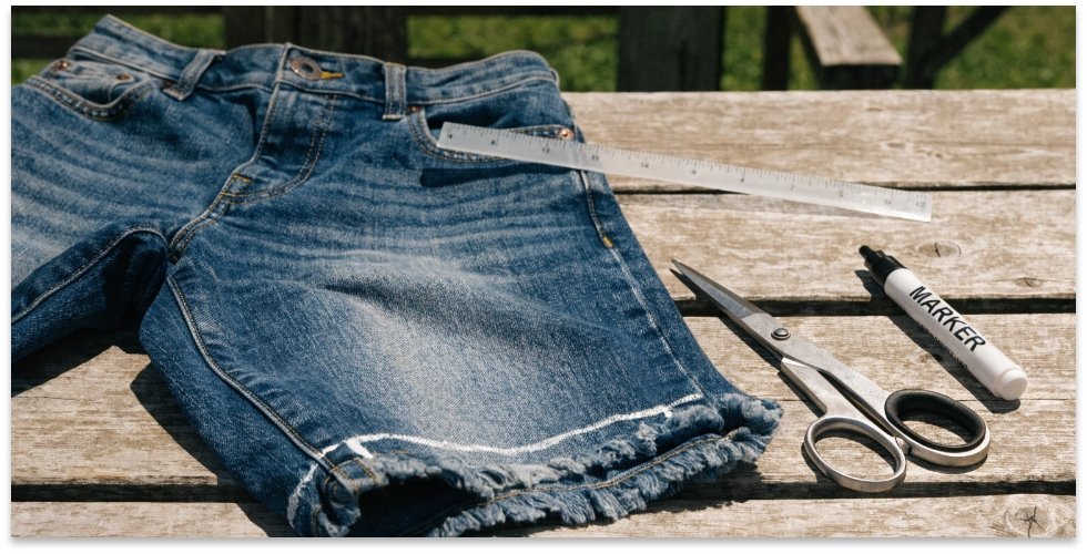 Tools for Cutting Jeans into Shorts A flat lay of a pair of jeans, scissors, a marker, and a ruler, ready for cutting.