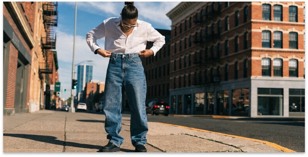 Checking jean fit with the 2 finger rule A person demonstrating the 2 finger rule on the waistband of their jeans.